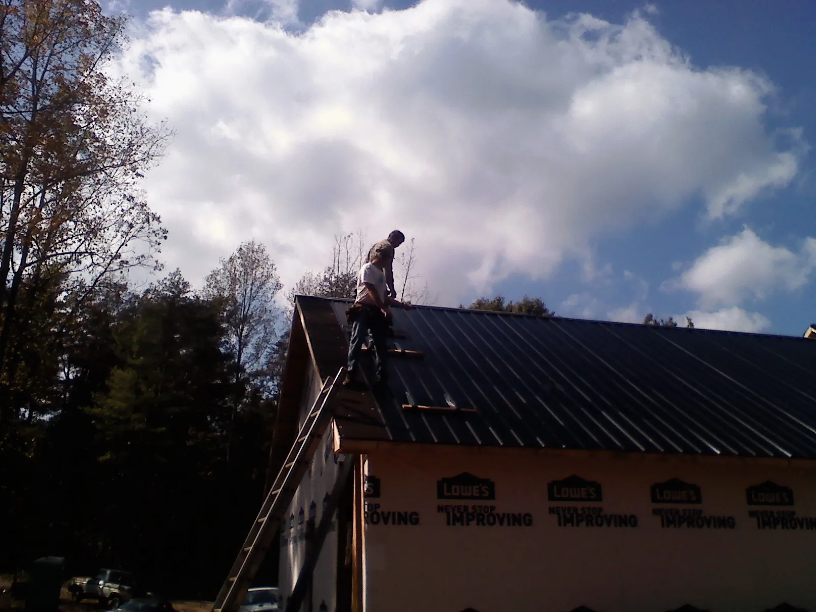 Roofer fastening dark metal panels high against a cloudy sky, from a Roof Inspection job in Hillsboro